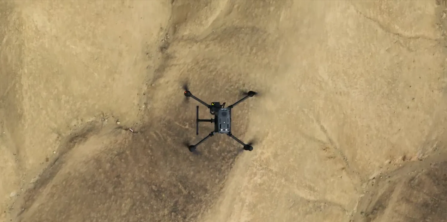 Top-down aerial view of a survey drone capturing photogrammetry imagery over terrain
